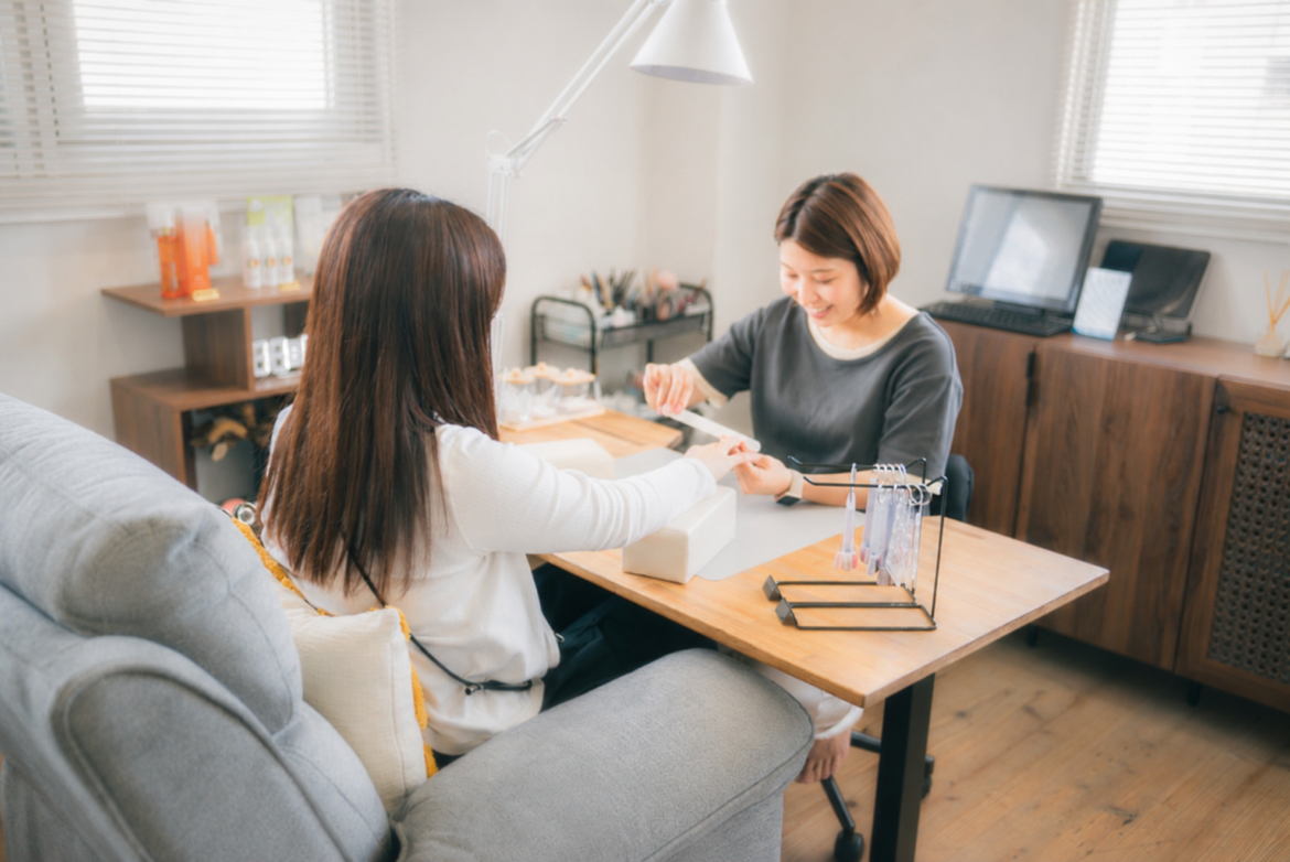 お客様と笑顔で会話をしながら、丁寧にネイルケアの施術を行うネイリスト