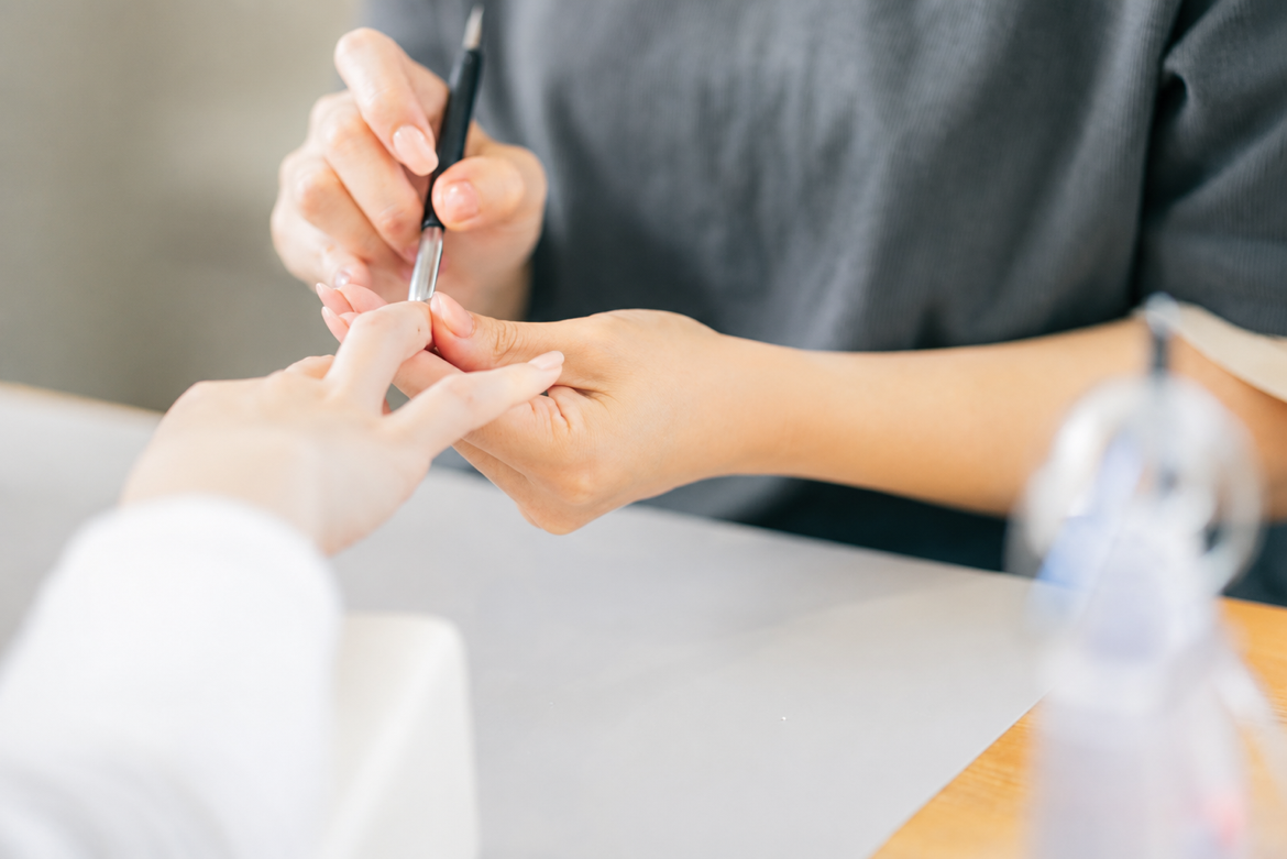 白手袋をしたネイリストが、細い筆を使って丁寧にネイルを施している手元