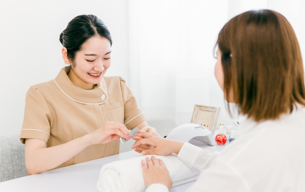 お客様と笑顔で会話をしながら、丁寧にネイルケアの施術を行うネイリスト